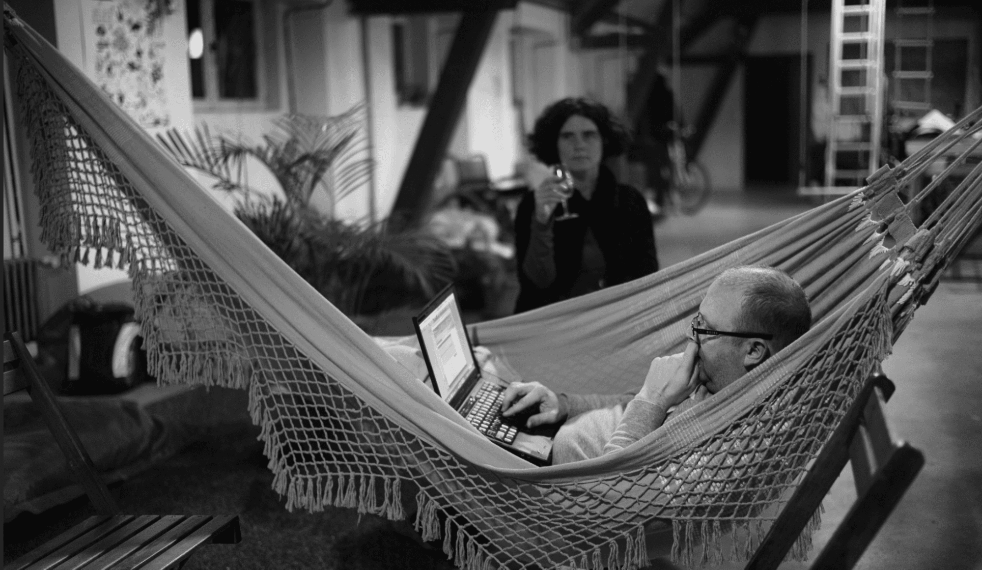 photo of man in hammock with laptop at a resort while woman looks on