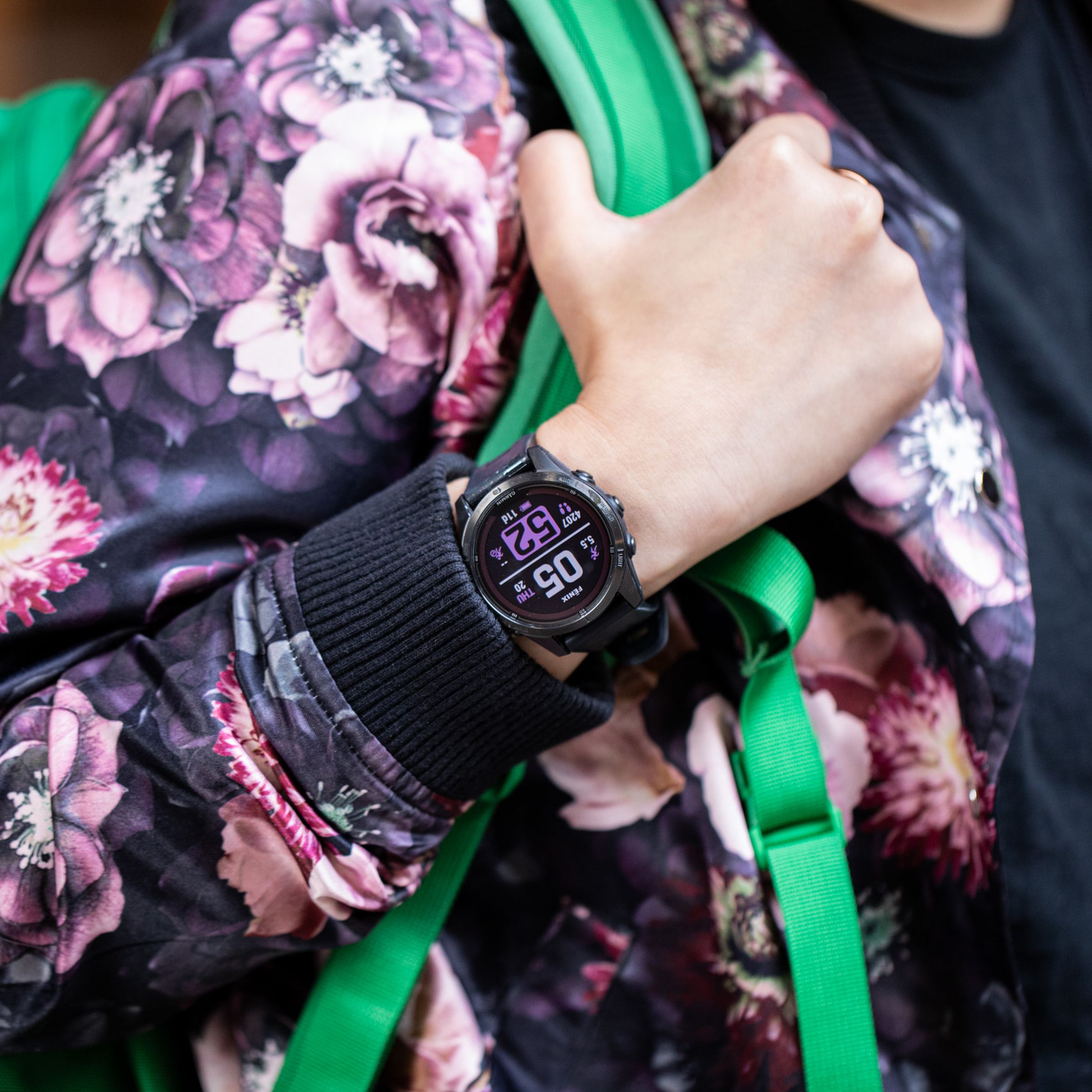 Person wearing a floral jacket and bright green backpack with a Garmin Fenix 7S Pro on their wrist
