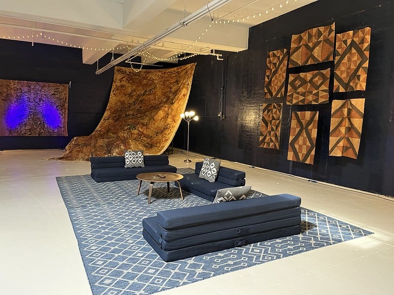 A large room, walls draped in fabric arts in earth tones. Comfortable lounge chairs arranged on a rug.